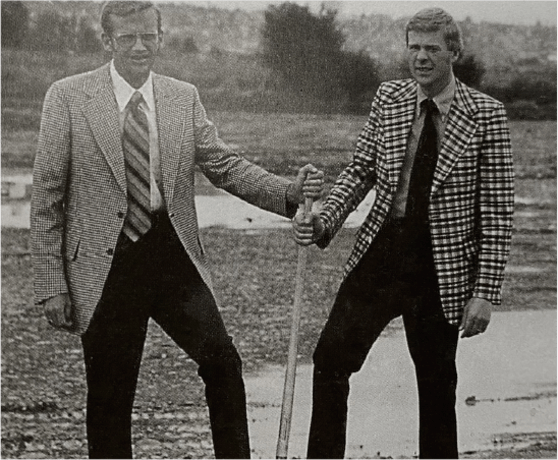 A black and white image of the Milgard brothers in suits, holding on to a shovel at a ground breaking.