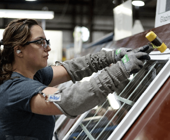 A woman to the left of the image wearing protective equipment is holding a hammer over a window laying on a work surface