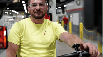  A man in a safety yellow shirt driving a forklift in a manufacturing plant