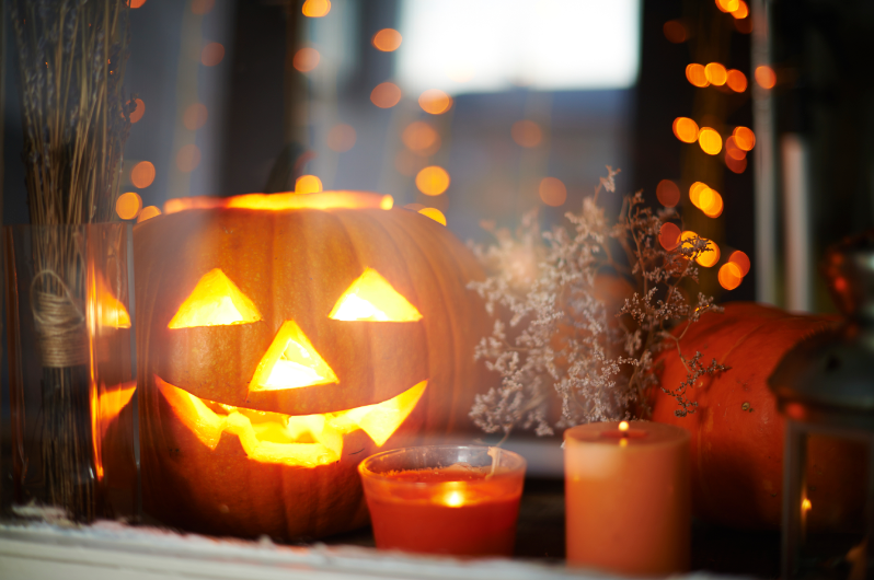 A Jack-O-Lantern Shines with Pillar Candles by the Window