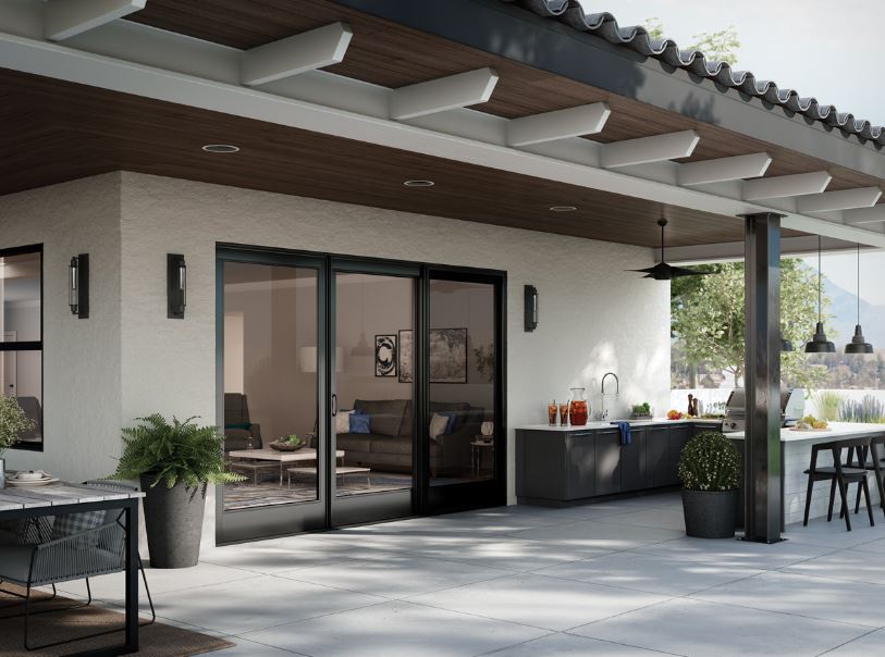 Dark Sliding glass patio doors are featured from an exterior view with a pergola covered patio with an outdoor kitchen with grill and wet bar.